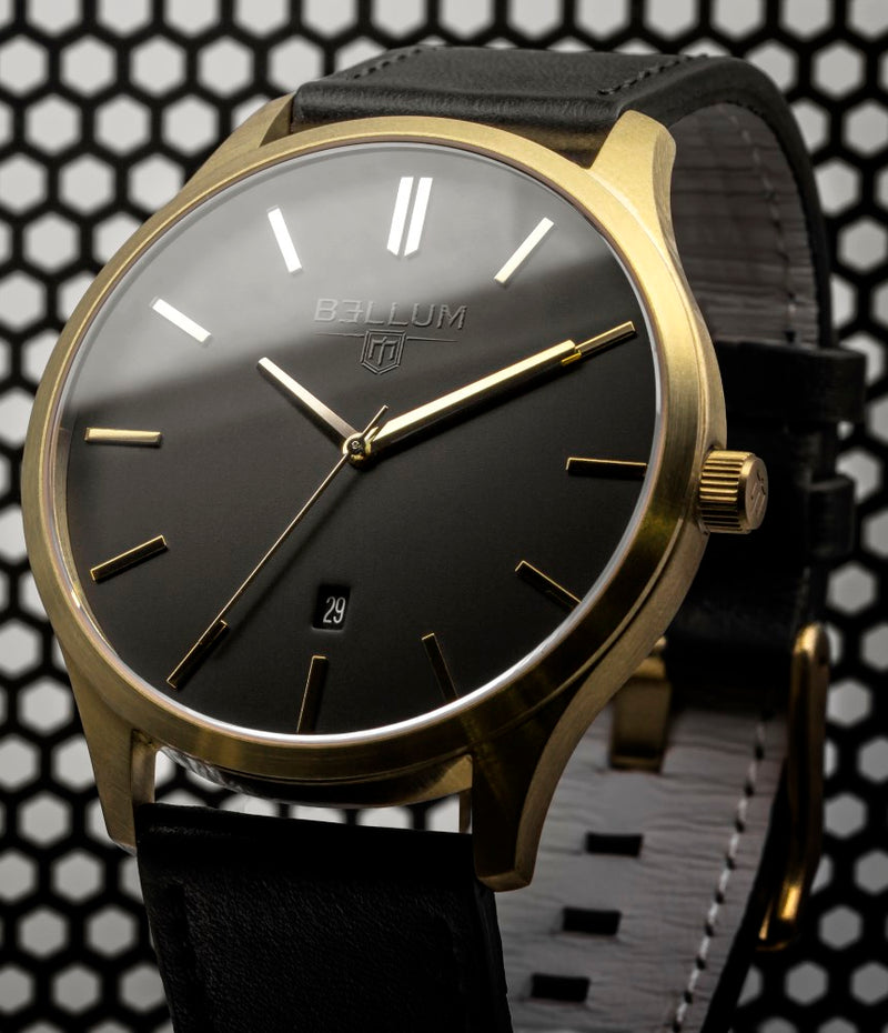 Reloj para hombre marca Bellum, color oro amarillo 14k en acabado cepillado con dial negro mate y correa de cuero negro. Vista semi-lateral en bodegón.